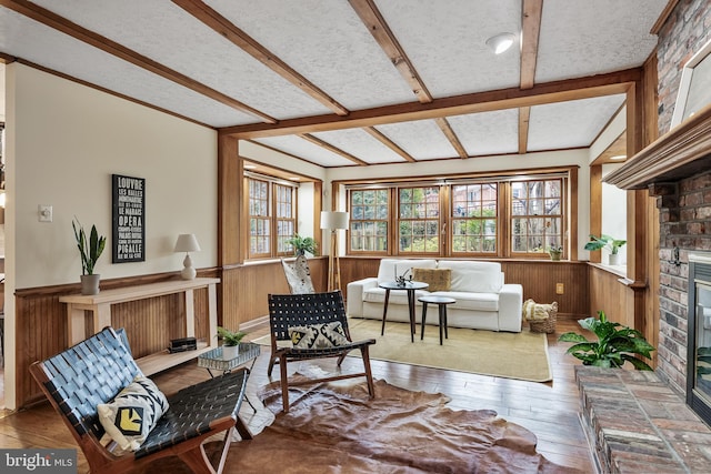 sitting room with beam ceiling, a fireplace, wood-type flooring, wainscoting, and a textured ceiling