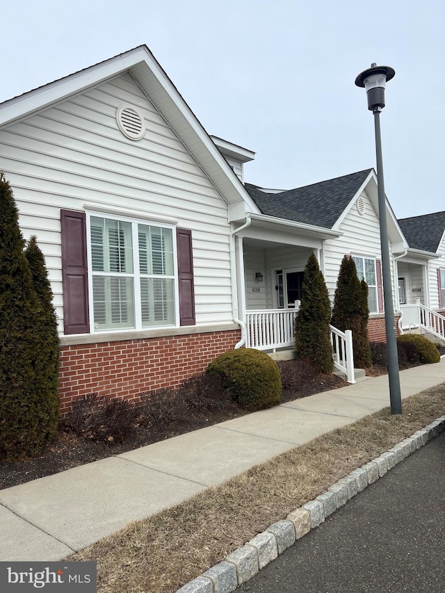 view of front of home with covered porch, a shingled roof, and brick siding