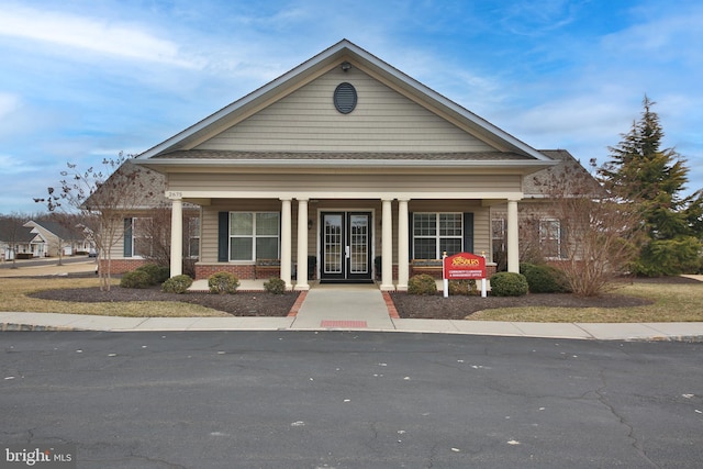 view of front of home with covered porch, brick siding, and french doors