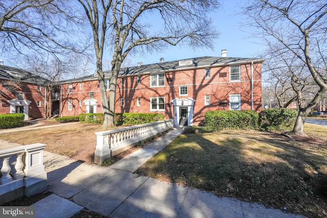 view of front facade featuring a front yard, a chimney, and brick siding