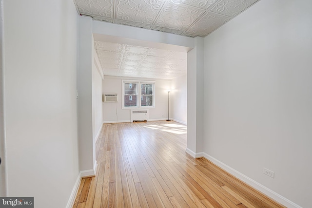 corridor with an ornate ceiling, a wall unit AC, radiator heating unit, light wood-style floors, and baseboards