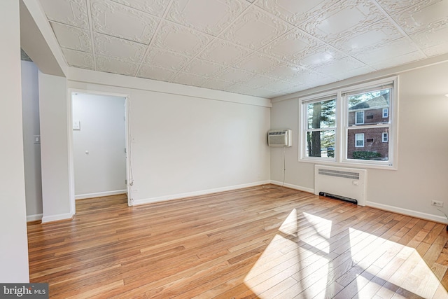 unfurnished room with baseboards, light wood-style floors, an AC wall unit, radiator heating unit, and an ornate ceiling