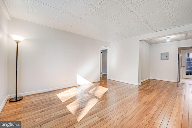 empty room with light wood-type flooring, electric panel, and baseboards