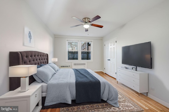 bedroom featuring baseboards, light wood finished floors, a wall mounted AC, and radiator