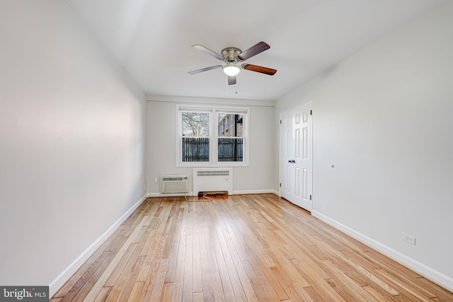 empty room featuring light wood finished floors, radiator, a ceiling fan, an AC wall unit, and baseboards