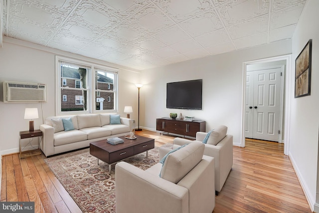 living area featuring light wood-style flooring, a wall mounted air conditioner, an ornate ceiling, and baseboards