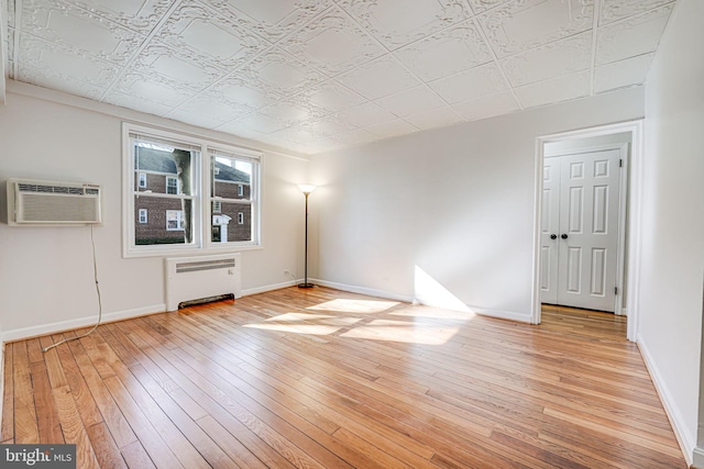 spare room featuring baseboards, a wall mounted AC, light wood-type flooring, radiator heating unit, and an ornate ceiling