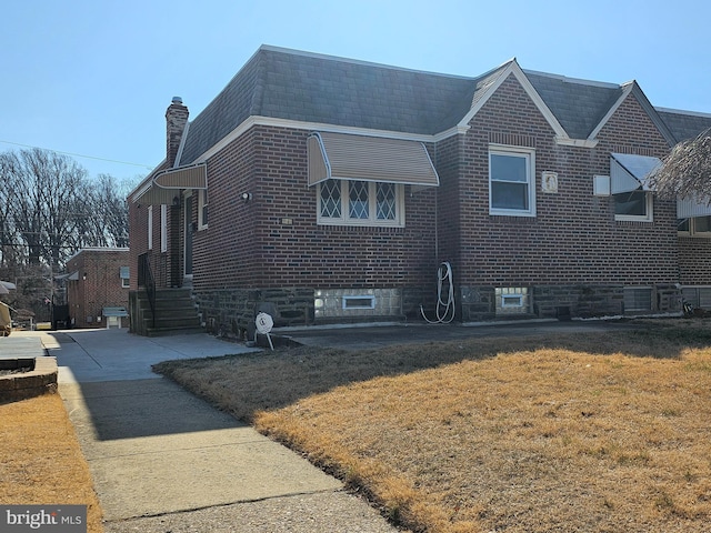 view of side of home with a yard, brick siding, a chimney, and a shingled roof