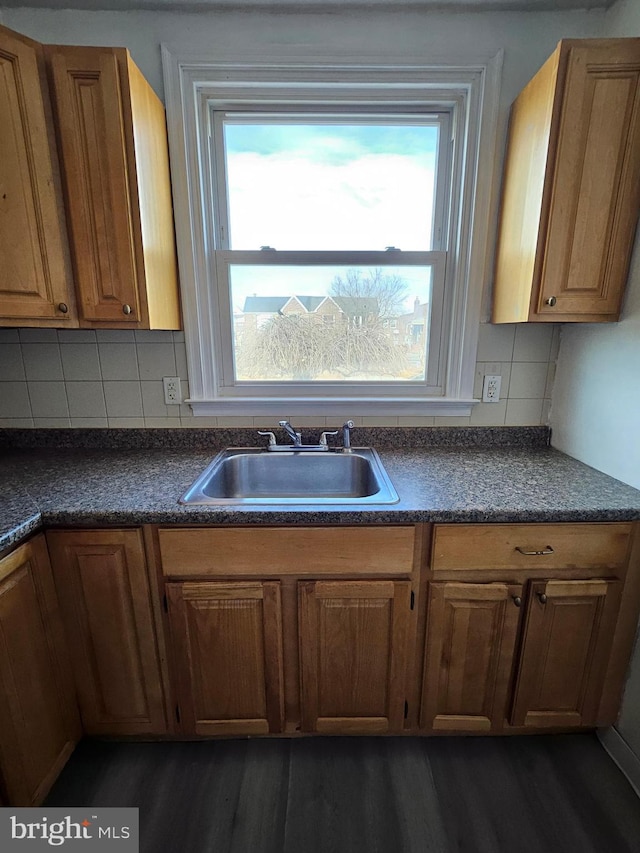 kitchen with dark wood finished floors, dark countertops, backsplash, brown cabinetry, and a sink