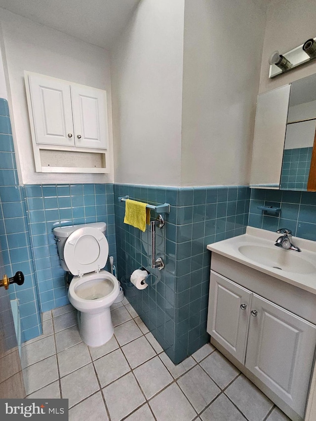 bathroom with tile patterned flooring, toilet, vanity, tile walls, and wainscoting