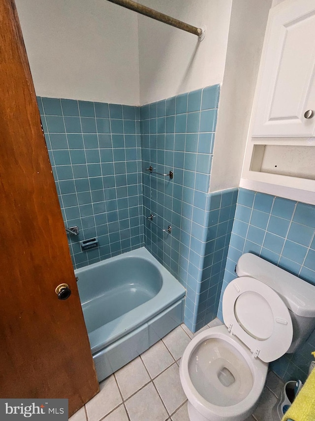 full bathroom with toilet, a wainscoted wall, tile patterned floors,  shower combination, and tile walls