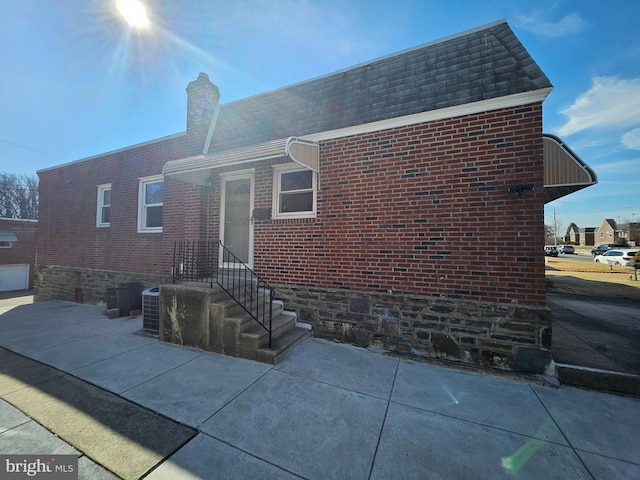 exterior space with roof with shingles, a chimney, mansard roof, and brick siding