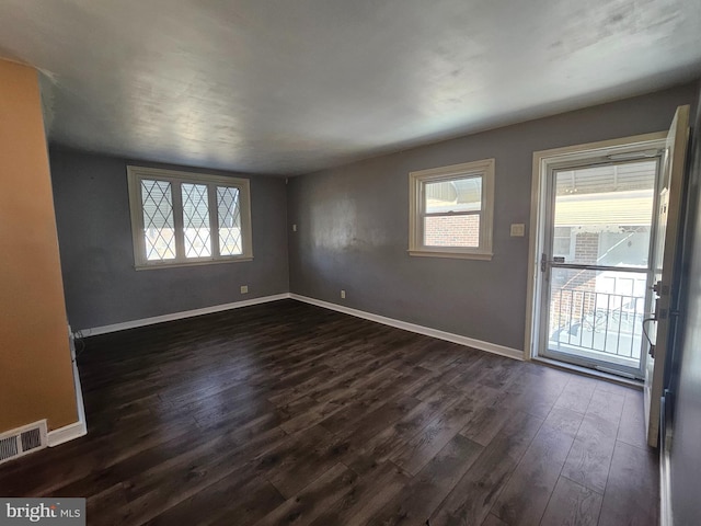 unfurnished room with dark wood-style floors, visible vents, a wealth of natural light, and baseboards