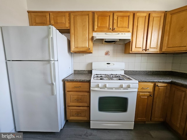 kitchen with white appliances, dark countertops, brown cabinets, and under cabinet range hood