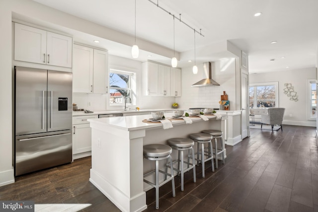 kitchen featuring light countertops, stainless steel built in refrigerator, white cabinetry, and wall chimney exhaust hood