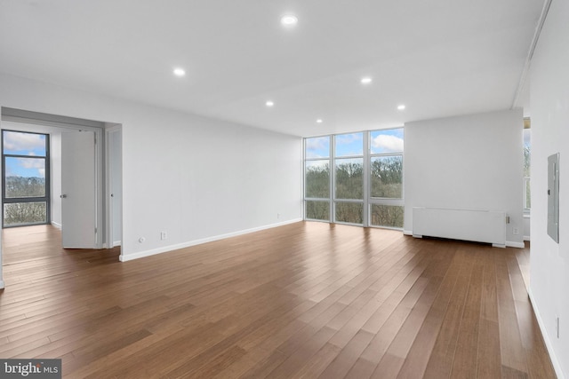 unfurnished living room featuring baseboards, radiator heating unit, wood finished floors, a wall of windows, and recessed lighting