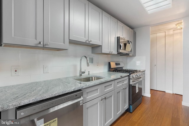 kitchen with light stone counters, a sink, stainless steel appliances, light wood-type flooring, and backsplash