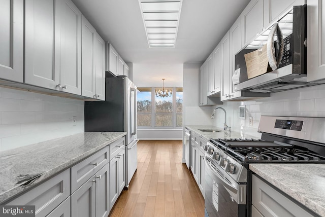 kitchen featuring stainless steel appliances, a sink, hanging light fixtures, backsplash, and light stone countertops