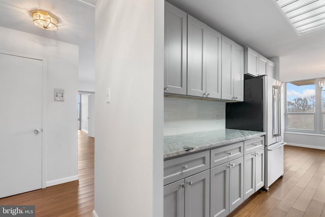 kitchen featuring light stone counters, backsplash, wood finished floors, and freestanding refrigerator