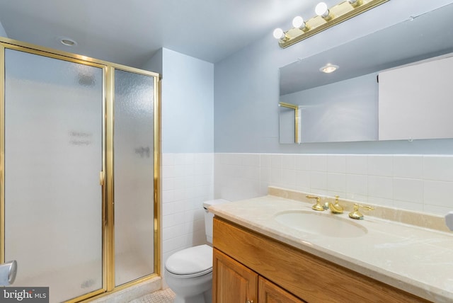 full bathroom with a stall shower, wainscoting, toilet, vanity, and tile walls