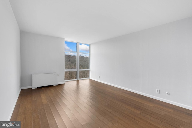 spare room featuring baseboards, floor to ceiling windows, wood finished floors, and radiator