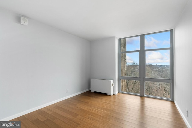 empty room featuring light wood-type flooring, radiator heating unit, floor to ceiling windows, and baseboards