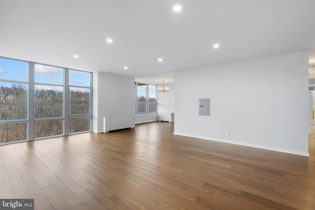 unfurnished living room featuring recessed lighting, electric panel, dark wood-style floors, radiator heating unit, and an inviting chandelier