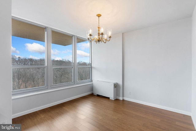 empty room featuring radiator, a notable chandelier, baseboards, and wood finished floors