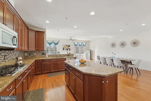kitchen with a kitchen island, a sink, light wood-style floors, appliances with stainless steel finishes, and backsplash