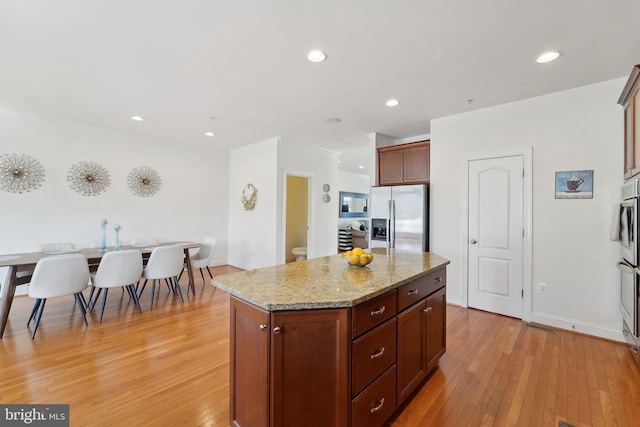 kitchen with light wood finished floors, a center island, light stone countertops, stainless steel refrigerator with ice dispenser, and recessed lighting