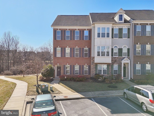 townhome / multi-family property featuring uncovered parking, brick siding, and a front yard