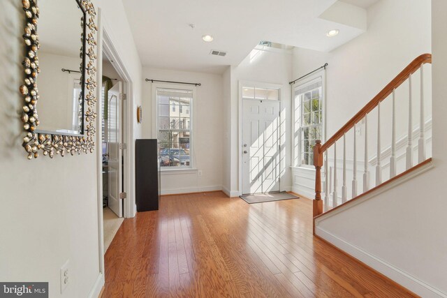 foyer entrance featuring stairway, wood-type flooring, visible vents, and baseboards