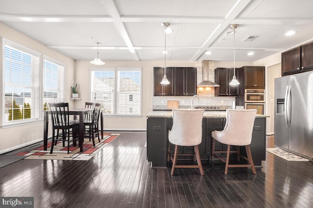 kitchen with pendant lighting, a center island with sink, stainless steel appliances, wall chimney range hood, and light stone countertops