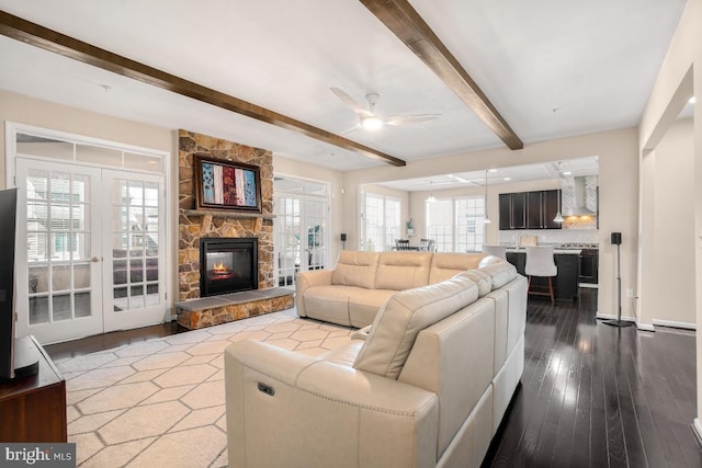 living room featuring beam ceiling, french doors, a fireplace, a ceiling fan, and wood finished floors