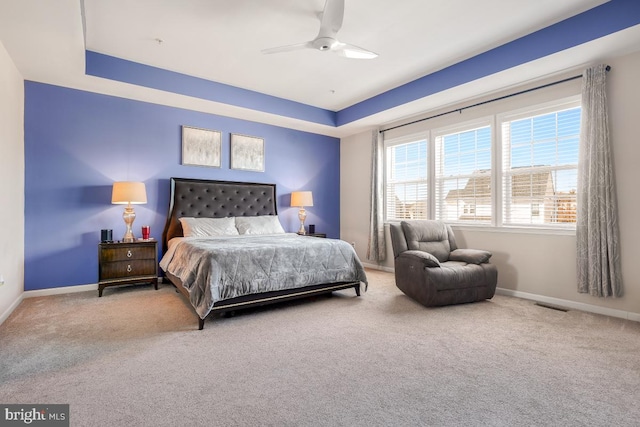 carpeted bedroom featuring a ceiling fan, a tray ceiling, visible vents, and baseboards