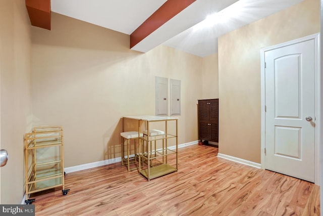 additional living space with baseboards, electric panel, beam ceiling, and light wood-style floors