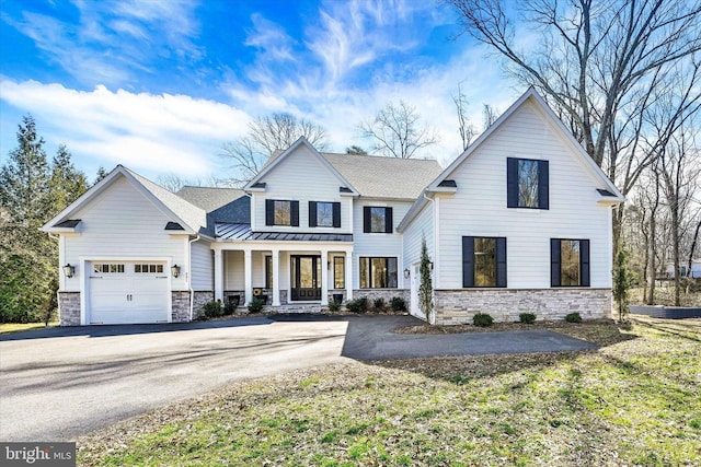 modern inspired farmhouse with a standing seam roof, covered porch, a garage, stone siding, and metal roof