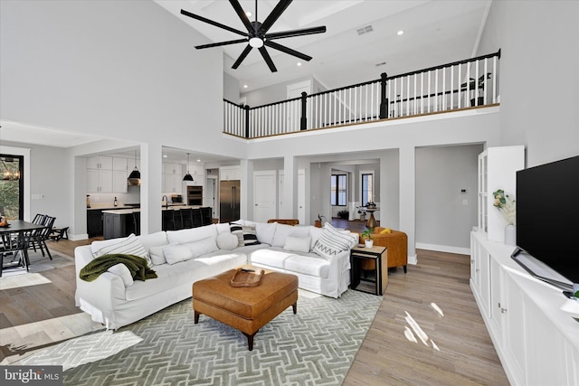 living room with ceiling fan with notable chandelier, recessed lighting, light wood-style floors, and baseboards