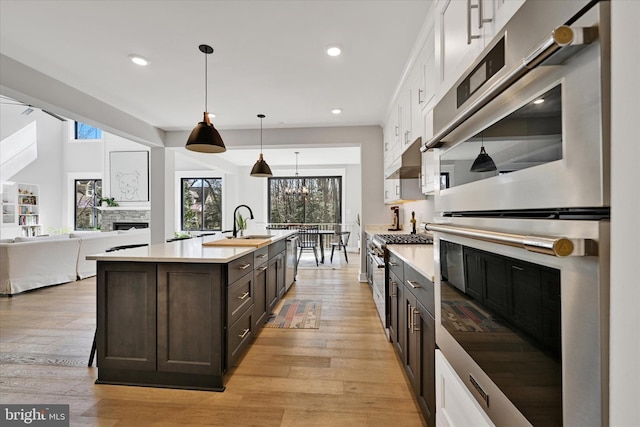 kitchen featuring a fireplace, dark brown cabinetry, white cabinets, light countertops, and appliances with stainless steel finishes