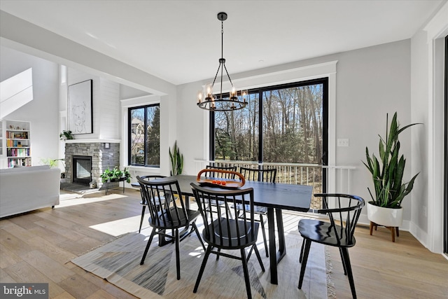 dining room featuring an inviting chandelier, a fireplace, light wood-type flooring, and baseboards