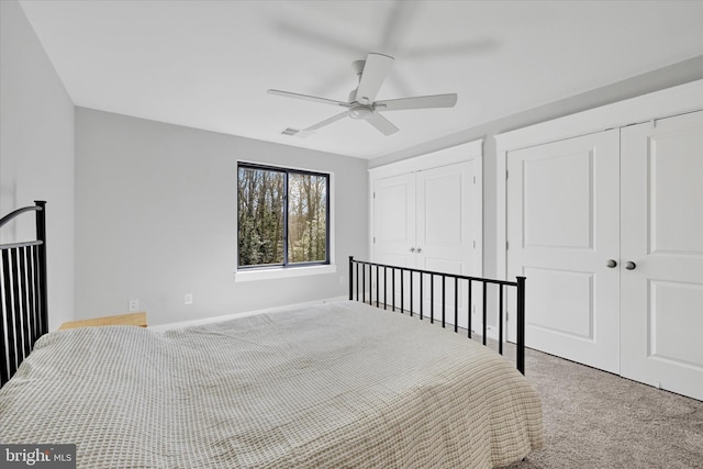 carpeted bedroom featuring visible vents, multiple closets, baseboards, and a ceiling fan