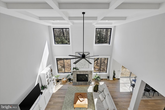 living room with light wood-style flooring, ceiling fan, coffered ceiling, a fireplace, and a towering ceiling