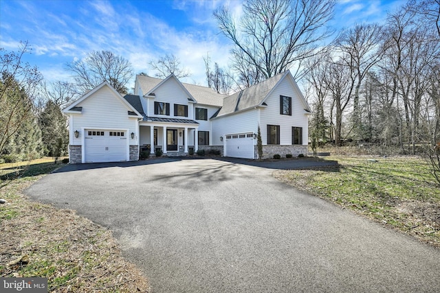 view of front facade with aphalt driveway, metal roof, a garage, stone siding, and a standing seam roof