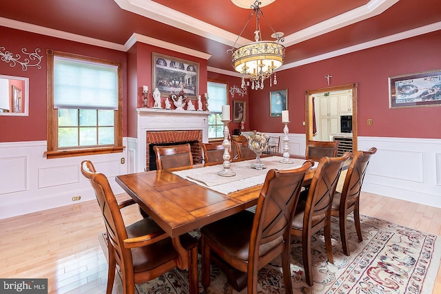 dining room with light wood-type flooring, a tray ceiling, and wainscoting