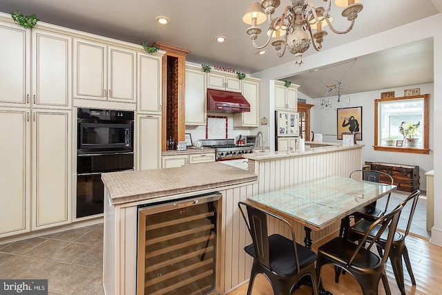 kitchen featuring cream cabinets, wall oven, an island with sink, beverage cooler, and extractor fan