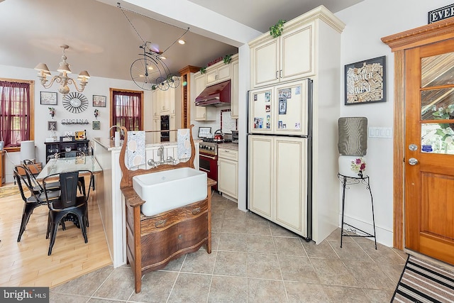 kitchen with paneled refrigerator, under cabinet range hood, range with gas stovetop, cream cabinetry, and pendant lighting