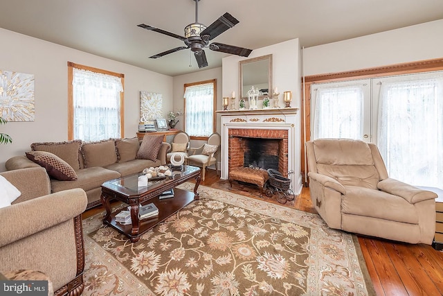 living room featuring a brick fireplace, wood finished floors, and a ceiling fan