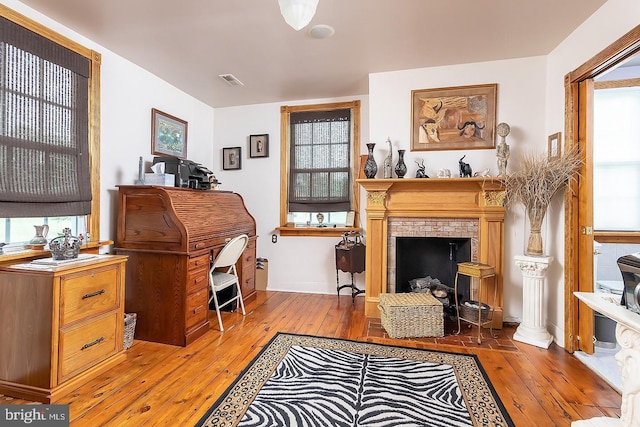 living area featuring light wood-style floors, a brick fireplace, and visible vents