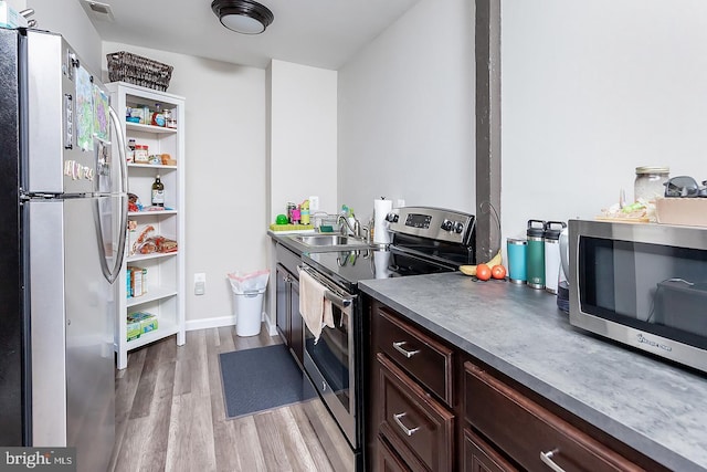 kitchen featuring stainless steel appliances, visible vents, a sink, dark brown cabinetry, and light wood-type flooring