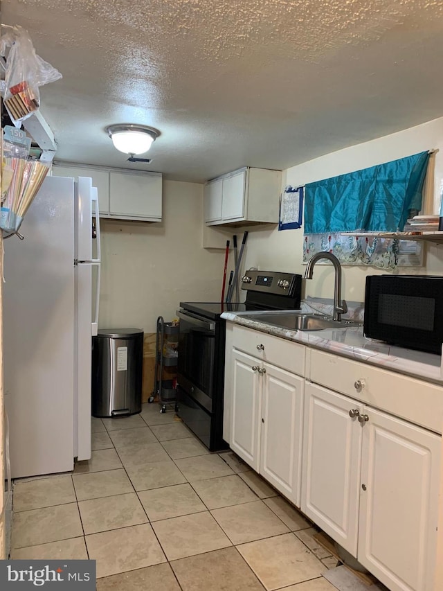 kitchen with black microwave, a sink, white cabinetry, electric stove, and freestanding refrigerator